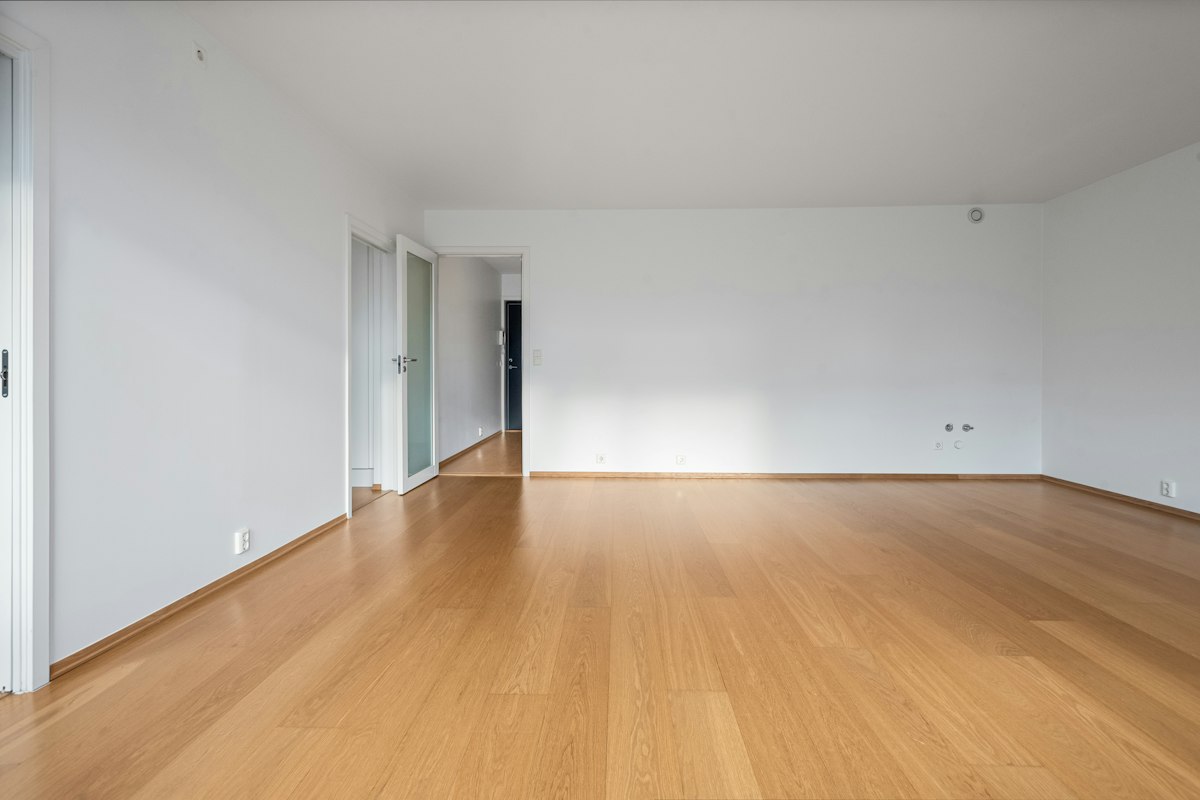 Sala de apartamento vazia, com piso de madeira, rodapés e paredes brancas, pronta para a vistoria de recebimento